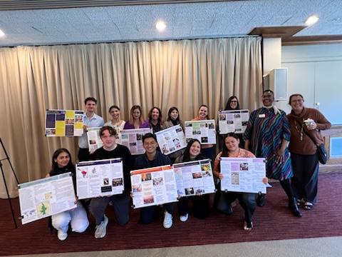 Students from the IR 550 class hold their presentation posters for the camera. They are standing and kneeling in rows, and are smiling. Dean Nwankwo and Professor Burcu Ellis stand to the right and smile at the camera.
