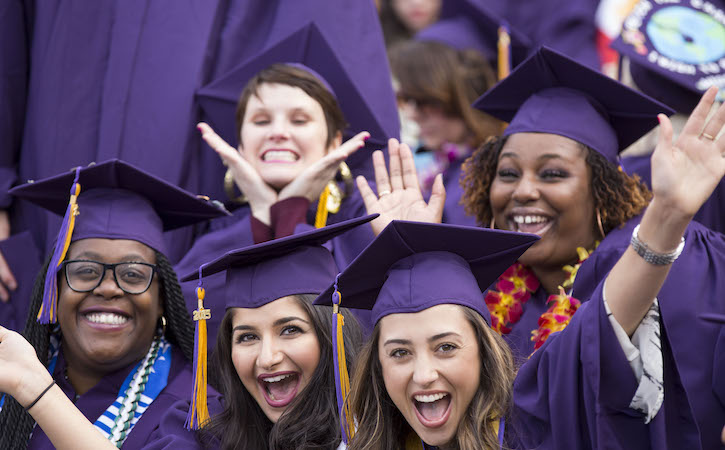 Outside five graduates dressed in purple gowns and hats smiling