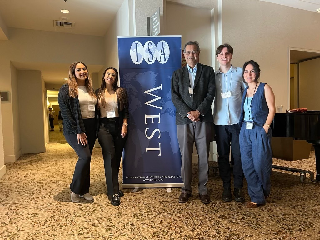 Professor Sanjoy Banerjee and 4 students stand around a purple ISA West banner and smile for the camera.