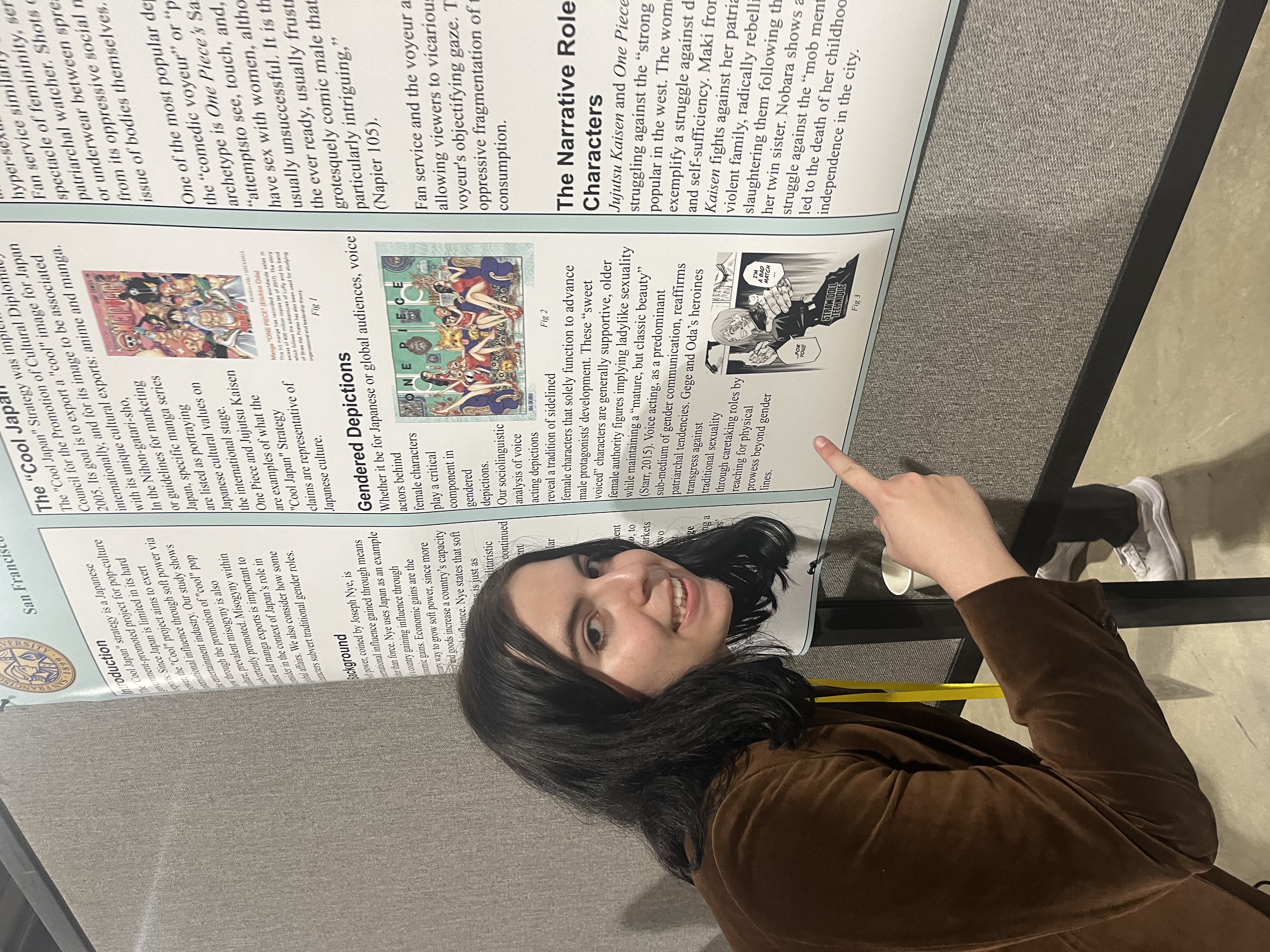 Tara Tara Shafie leans toward her poster. She is smiling and pointing at the content displayed there.